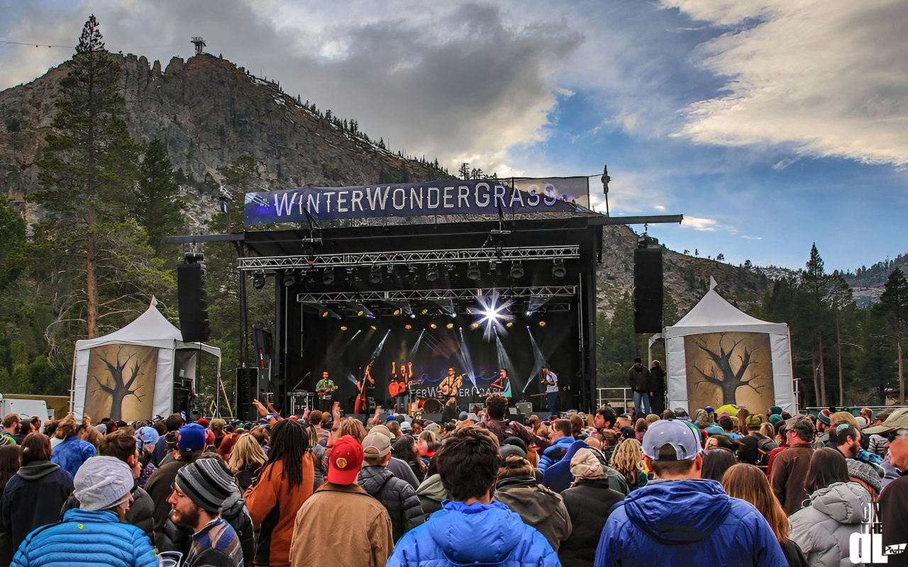 Crowd watching a live band at WinterWonderGrass, with forested mountains behind the outdoor stage.