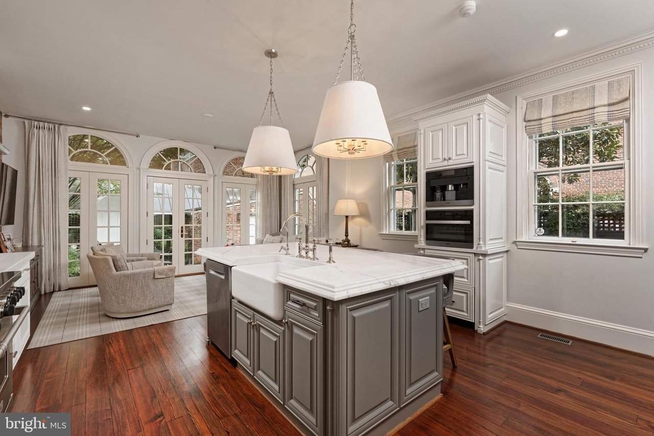 Bright kitchen with a marble island, farmhouse sink, white cabinetry, and arched French doors.
