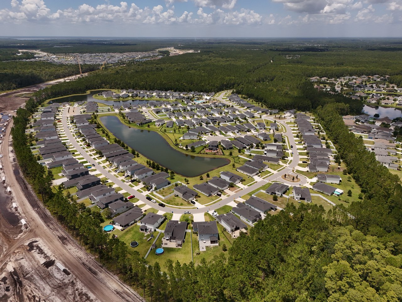 Aerial view of homes lining curving streets around a central pond, bordered by woodland.