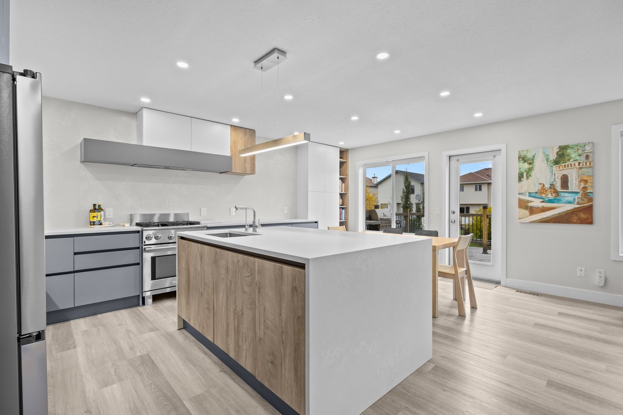 Modern kitchen with a large white island, gray cabinetry, and glass doors to a deck.
