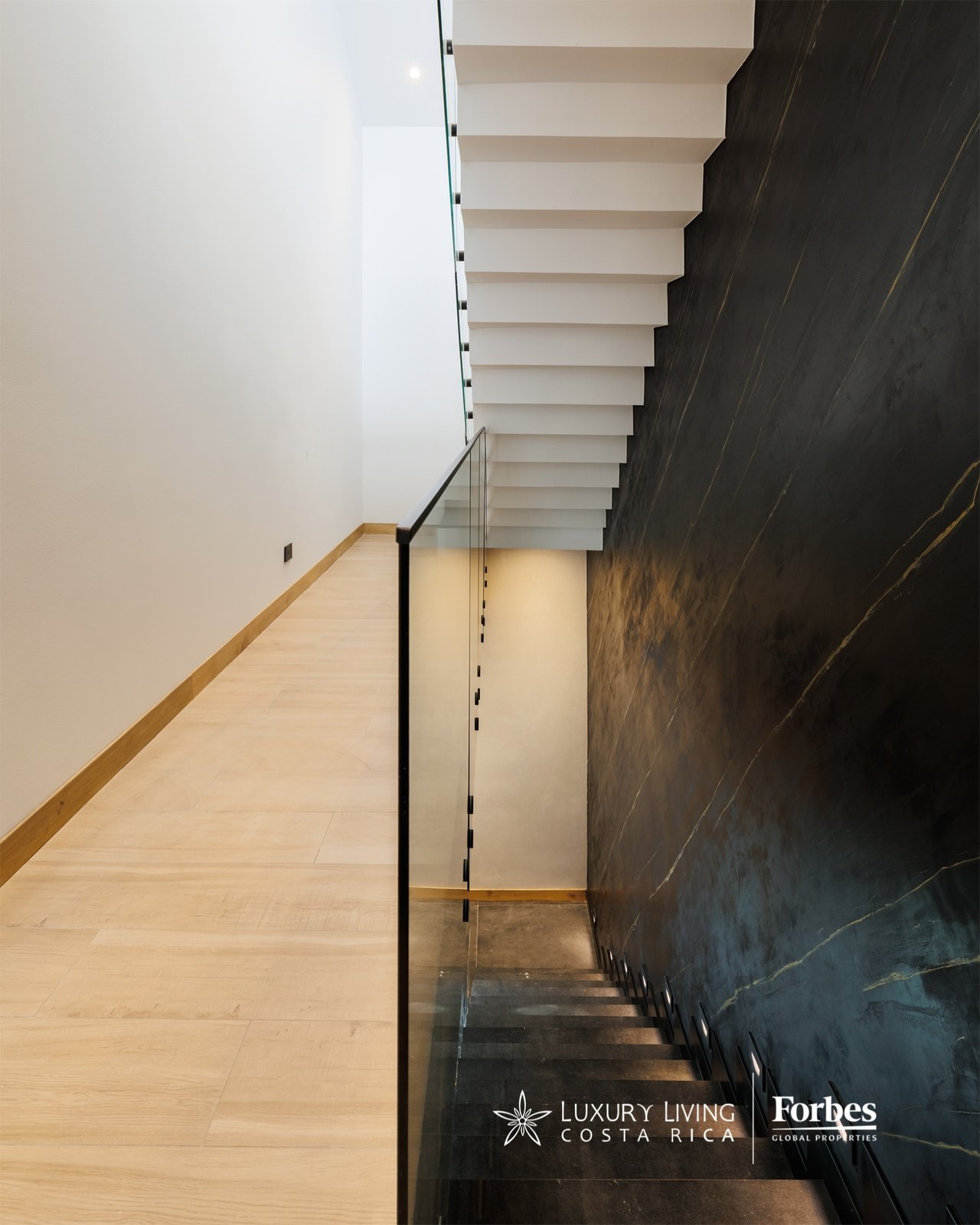 Modern staircase with floating white steps, glass railing, and dark veined stone wall.