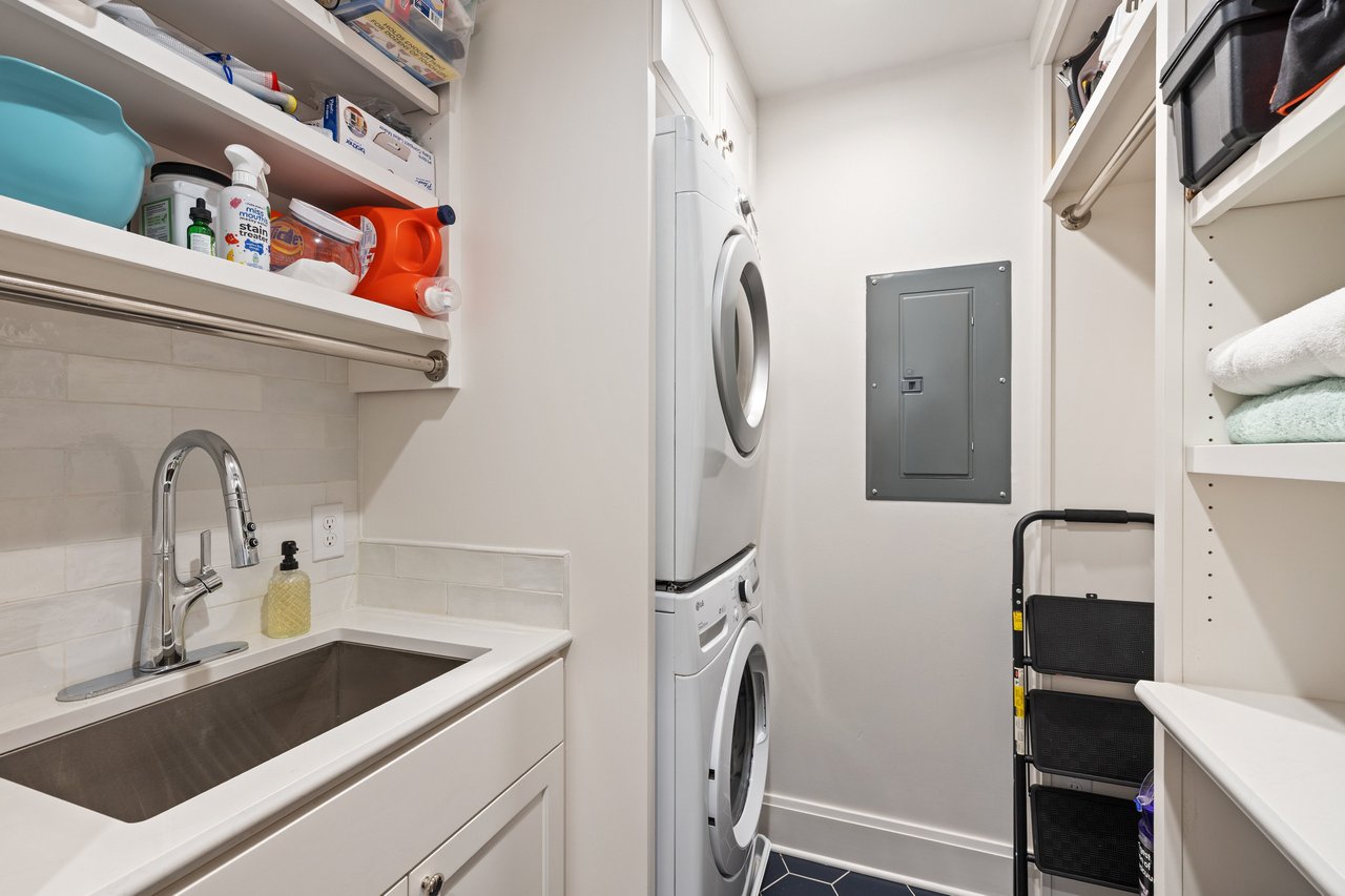 Laundry room with stacked washer and dryer, deep utility sink, and open storage shelves.