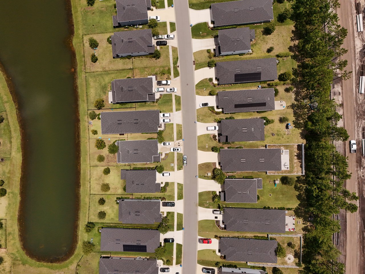 Aerial view of detached homes along a street beside a pond.