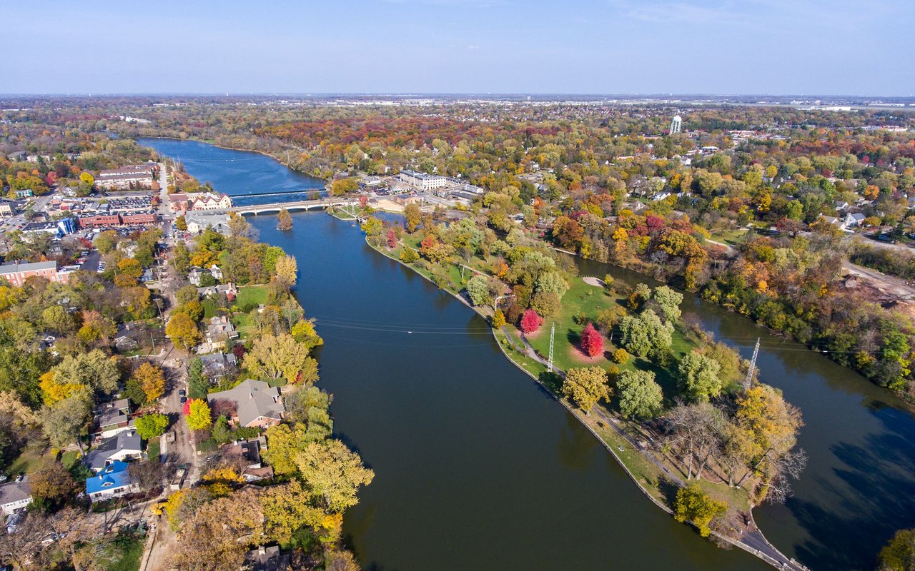 Aerial view of a river, bridge, homes, and autumn-colored parks.