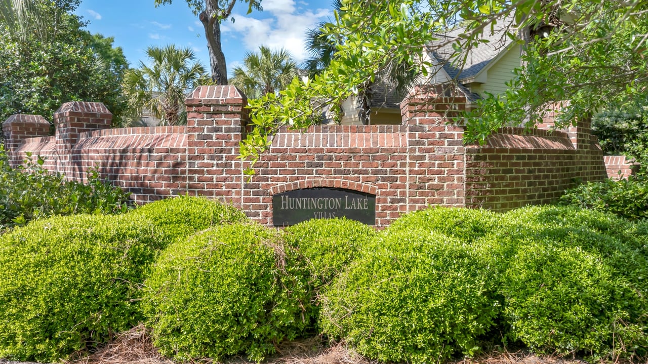 Huntington Lake Villas entrance sign in a brick wall behind lush hedges.