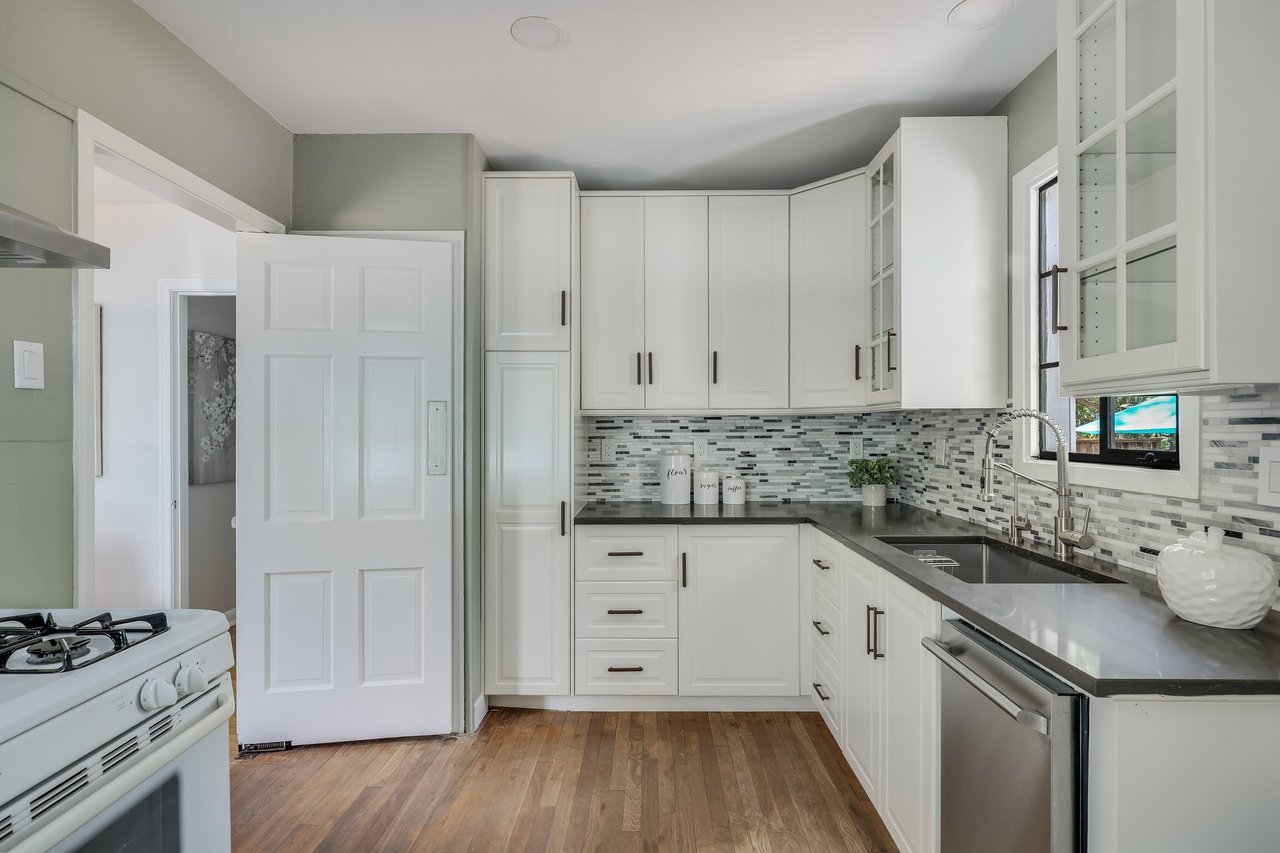 Kitchen with white shaker cabinets, gray mosaic backsplash, dark counters, and stainless steel dishwasher.