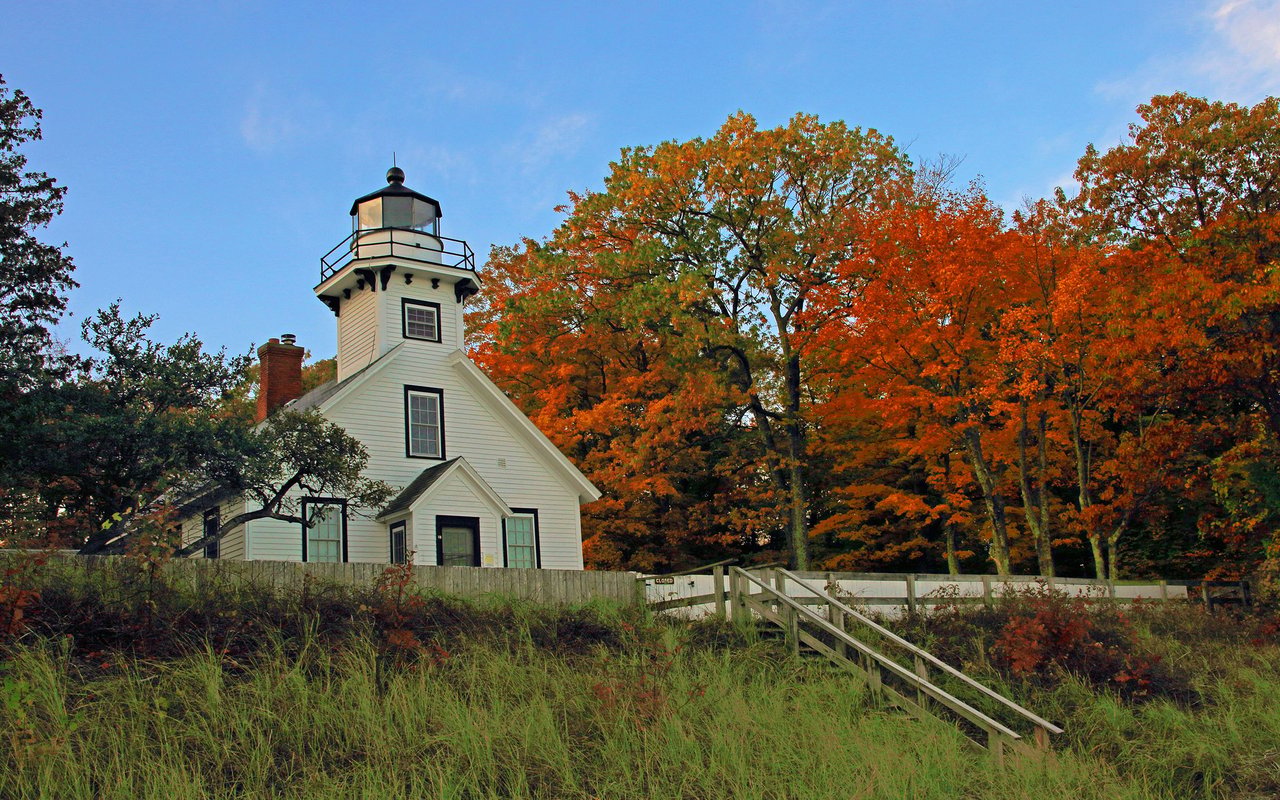 Old Mission Point Lighthouse framed by vivid autumn foliage and a white fence.