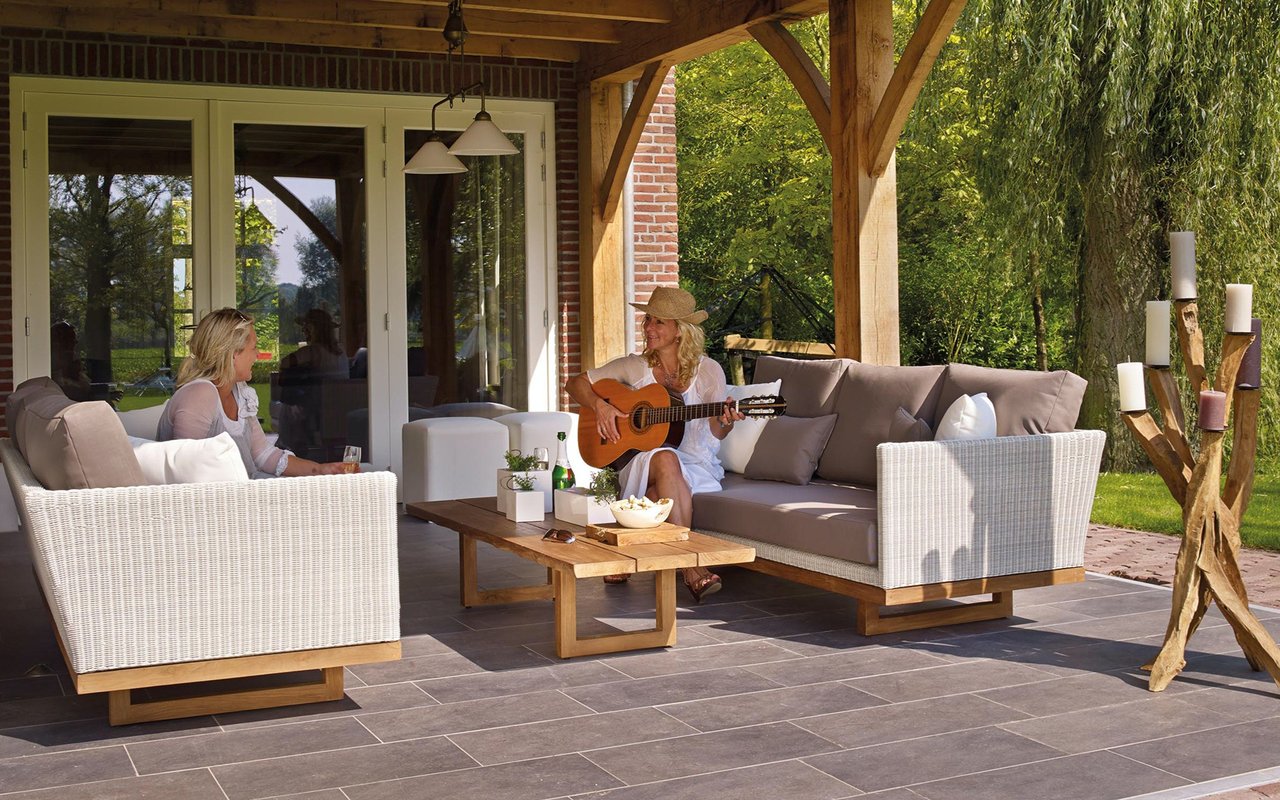 Covered patio with timber beams, wicker lounge seating, and sliding glass doors beside a garden.