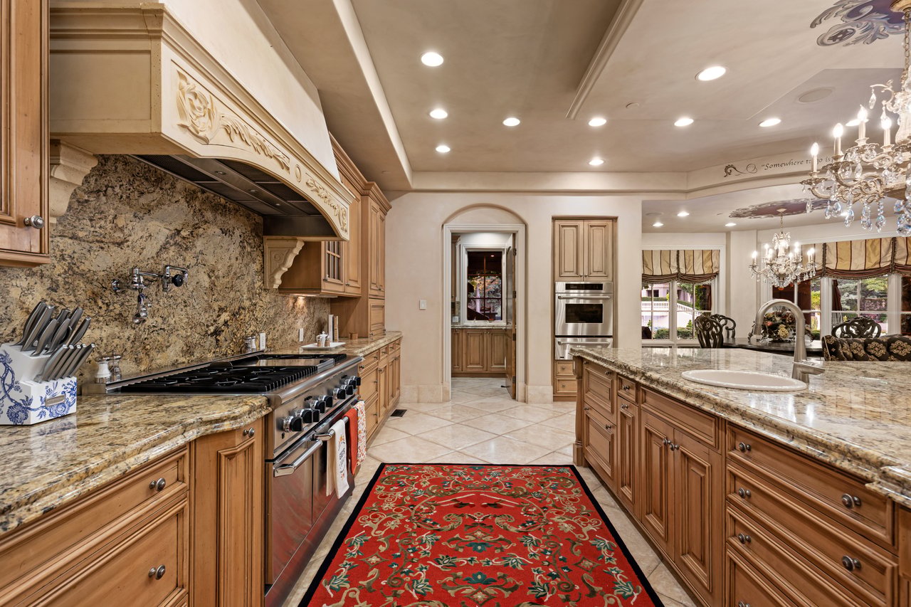 Kitchen with ornate wood cabinets, granite counters, a stainless-steel range, and a red patterned runner.