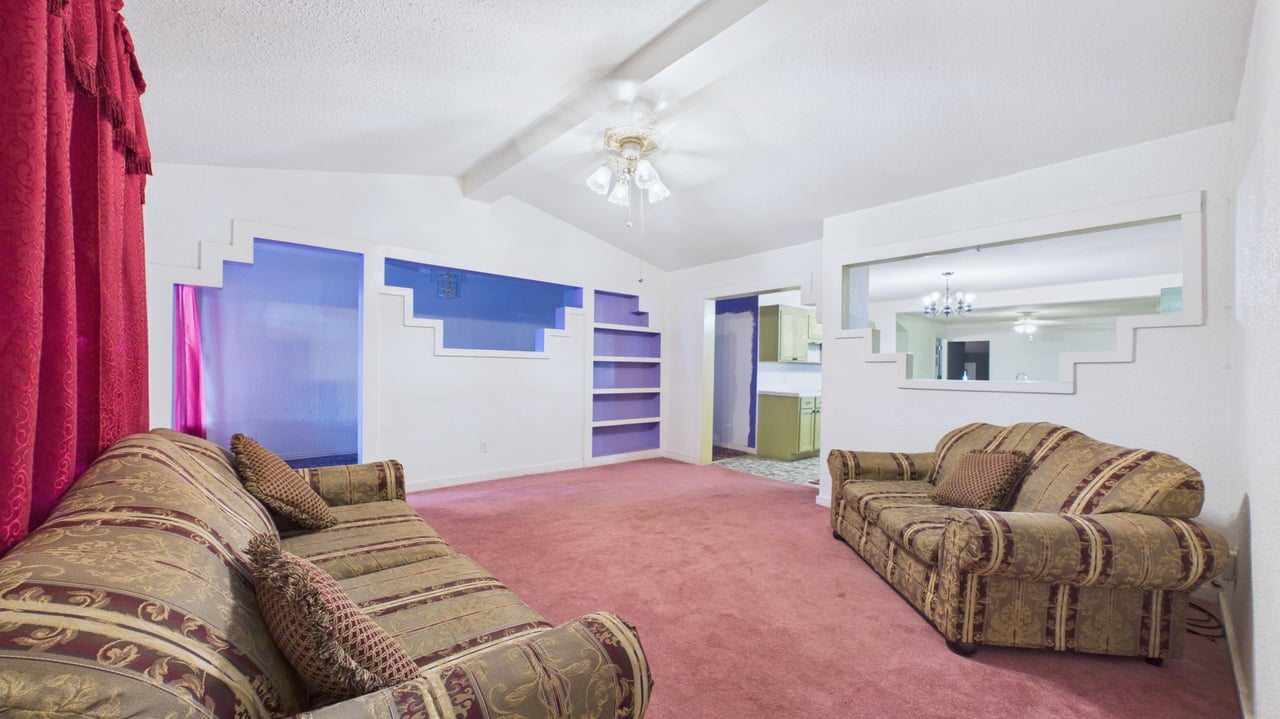 Living room with patterned sofas, pink carpet, built-in shelves, and a vaulted ceiling.