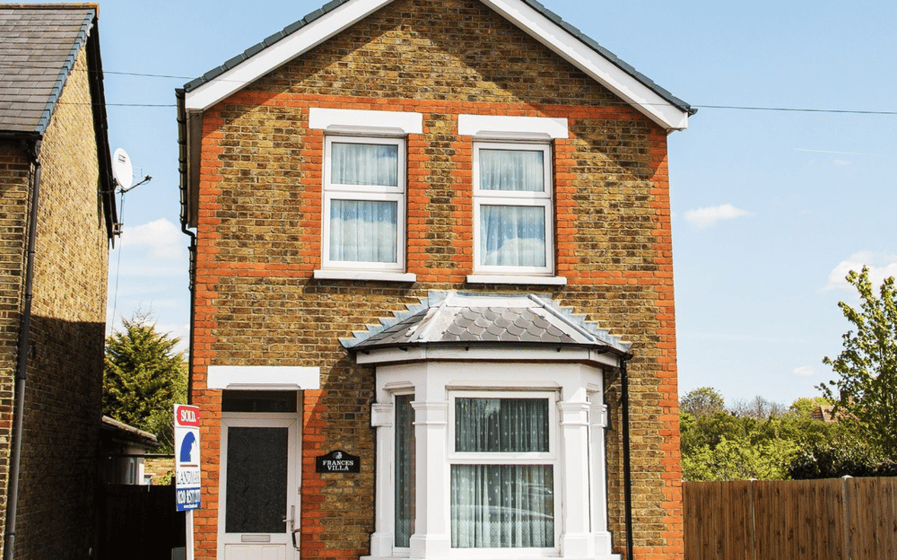 Brick house with white-trimmed windows and bay window, with a SOLD sign by the entrance.