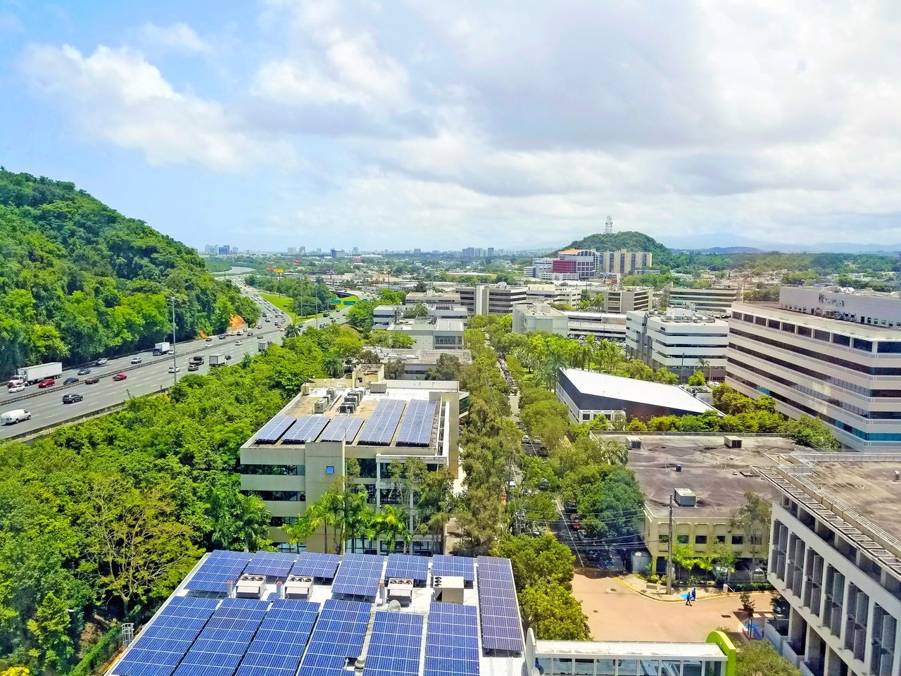 Aerial view of office buildings in Guaynabo surrounded by greenery, solar panels, and a highway.