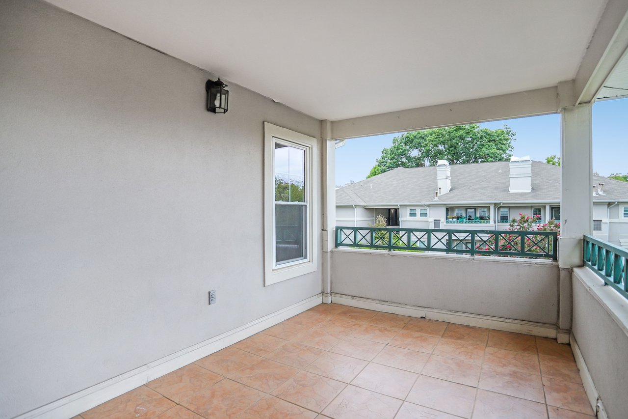 Covered balcony with peach tile flooring and green railings overlooking neighboring residences.