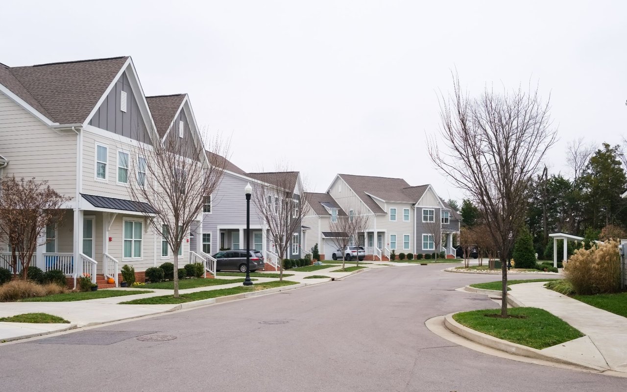 Residential street lined with attached homes, sidewalks, and leafless trees.