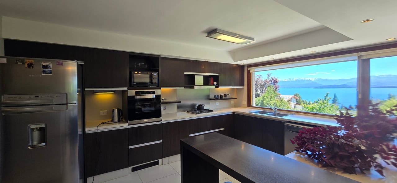 Modern kitchen with dark cabinets and a large window overlooking a lake and mountains.