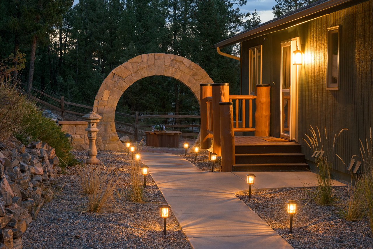 Wood-sided house entrance with a stone archway and illuminated walkway at dusk.