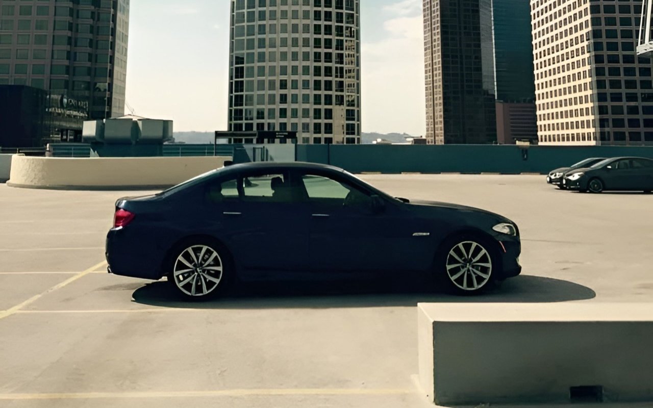 Dark sedan parked on a rooftop lot beneath downtown office towers.