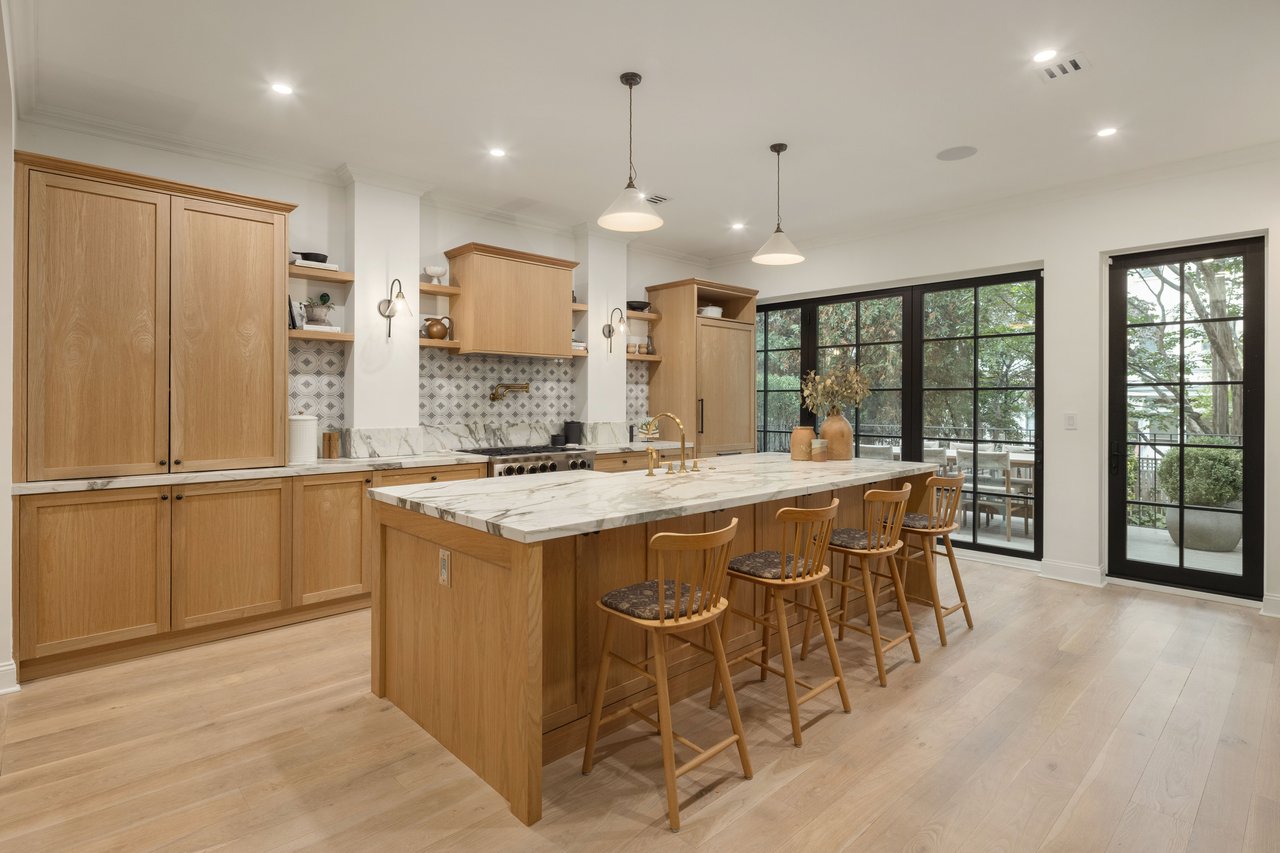 Modern oak kitchen featuring a marble island, wooden stools, and black glass doors