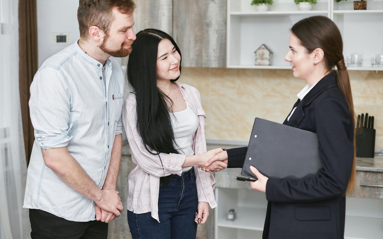 A couple talking to a real estate agent and smiling.