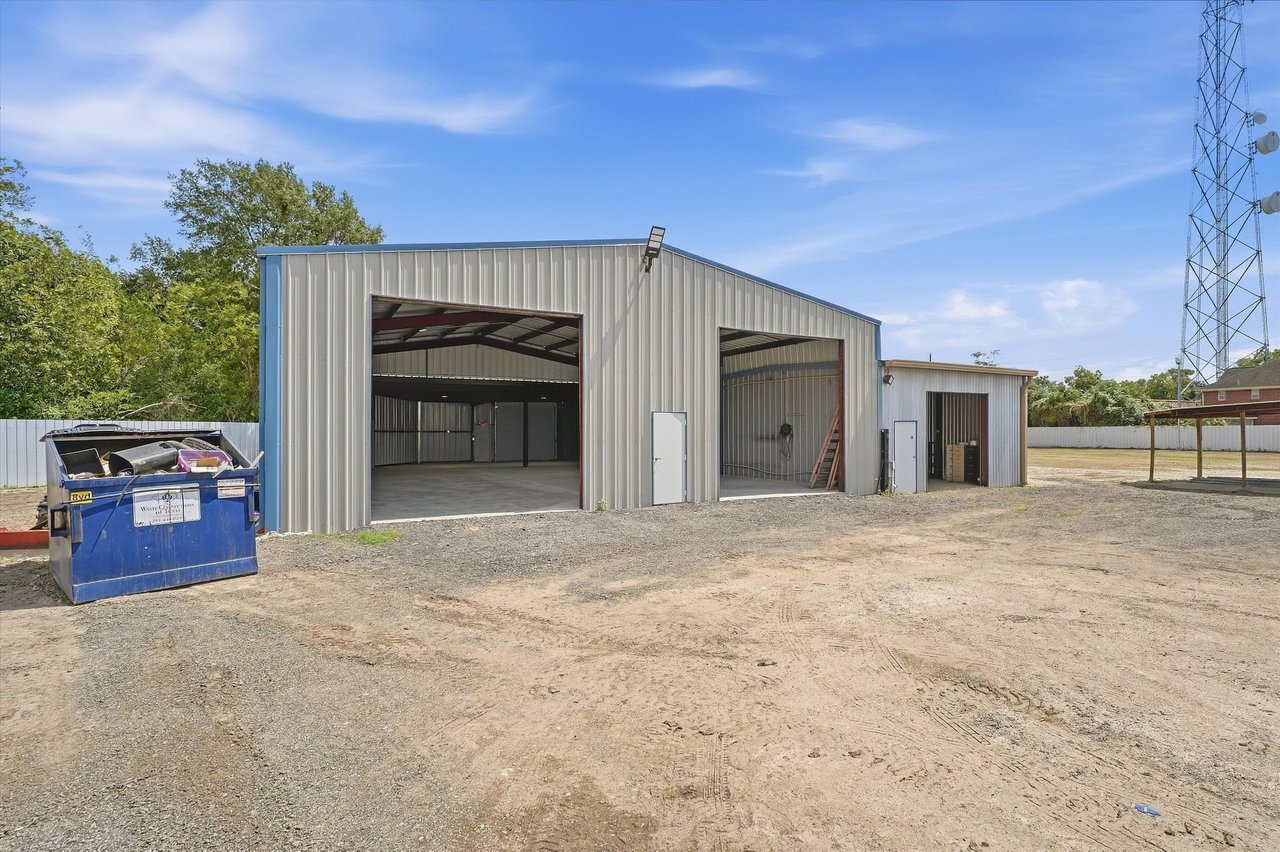 Metal workshop with two open bays beside a broad gravel yard and blue dumpster.