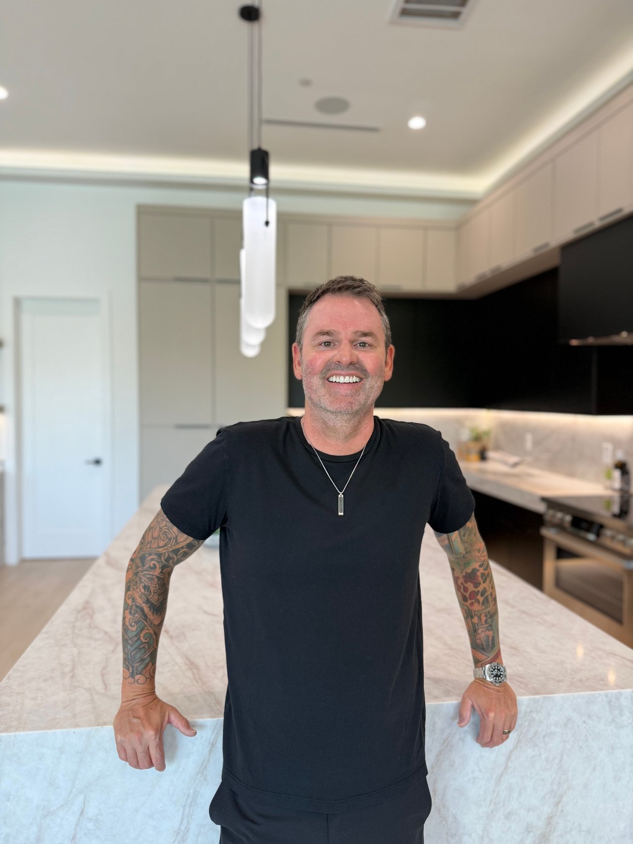 Bryce Hull smiling in a modern kitchen, his tattooed arms resting on a marble island.
