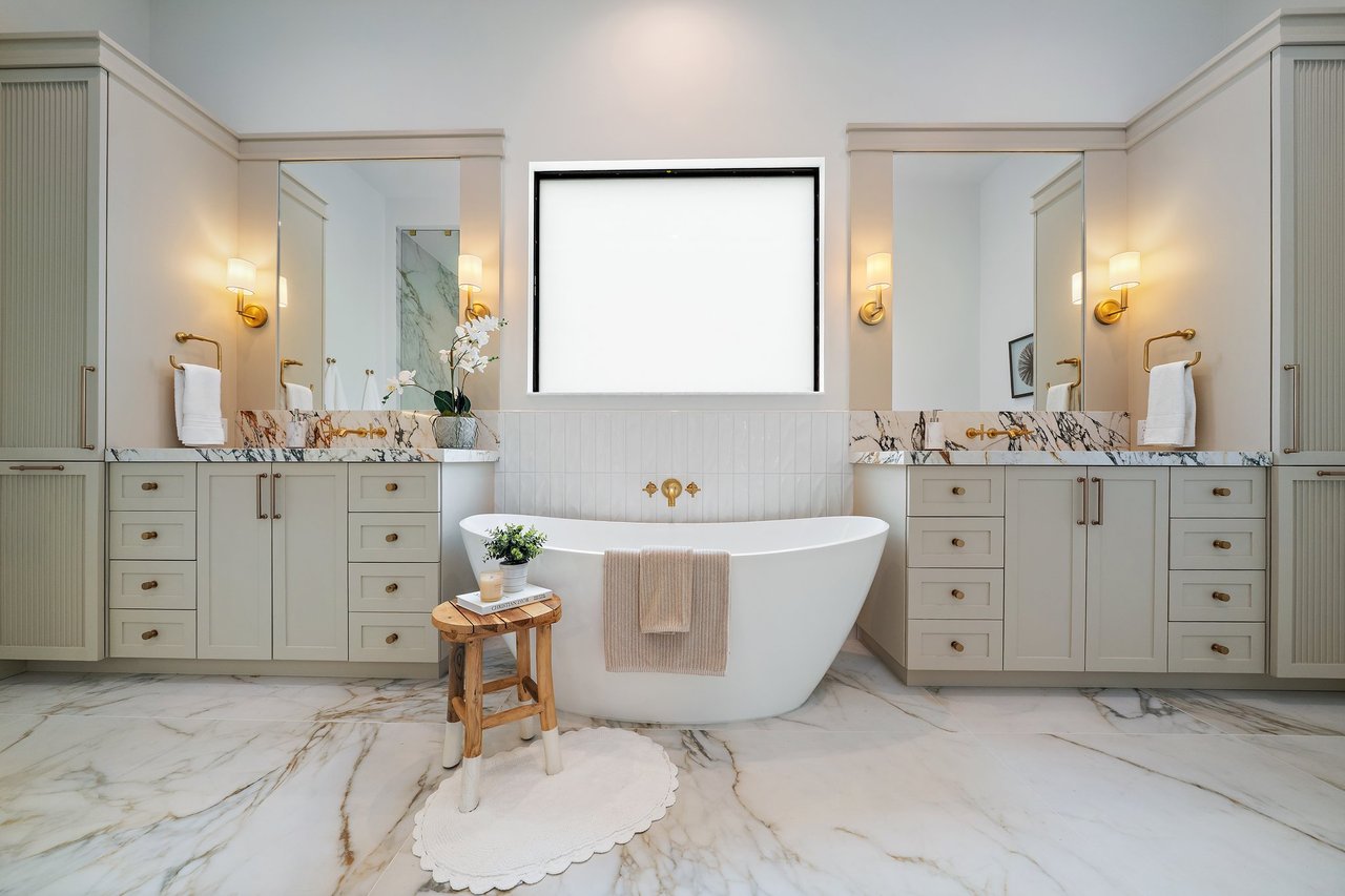 Bathroom with a freestanding soaking tub, dual vanities, marble surfaces, and brass fixtures.