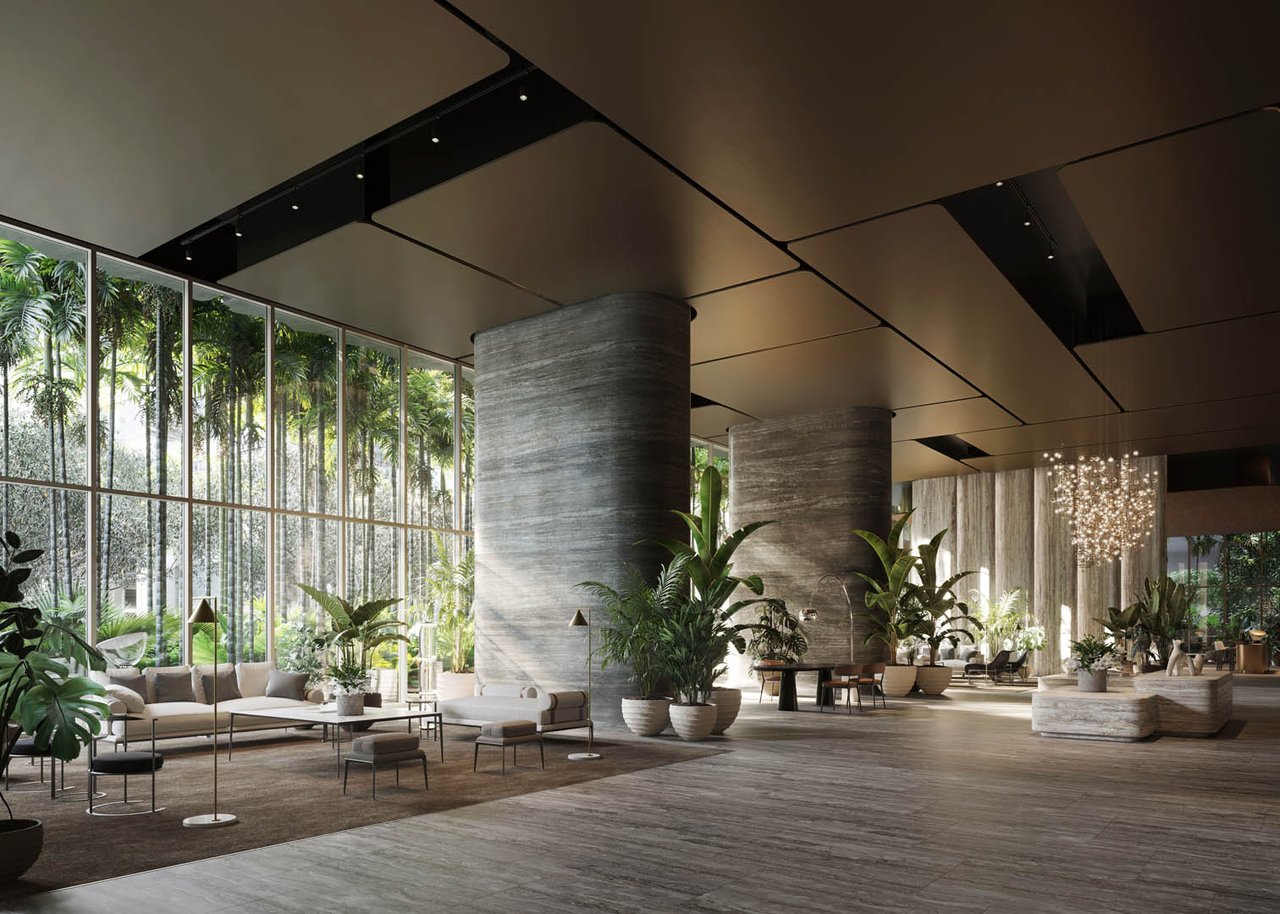 Residential lobby with floor-to-ceiling windows, tropical plants, stone columns, and lounge seating.