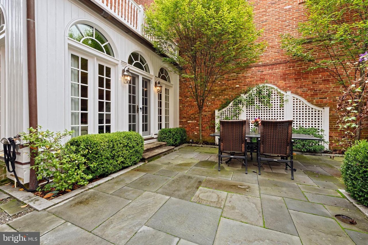 Private brick-walled courtyard with white French doors, leafy tree, and wicker patio dining set.