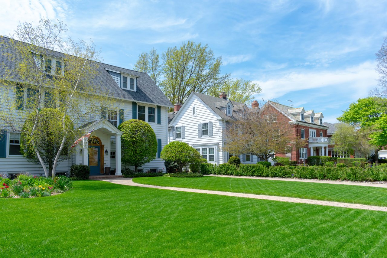 Suburban homes behind a broad green lawn, with mature trees and landscaped front yards.