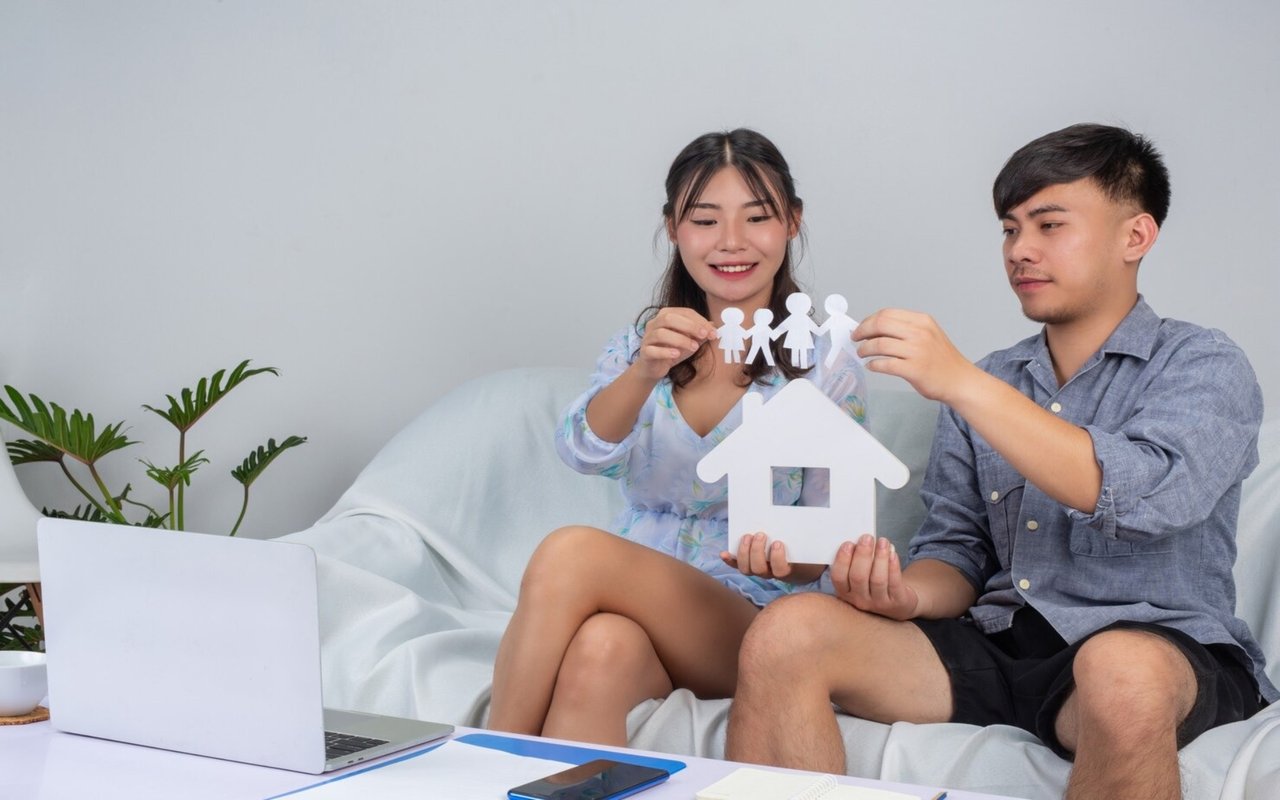 Couple planning a home purchase with a laptop and paper family and house cutouts.