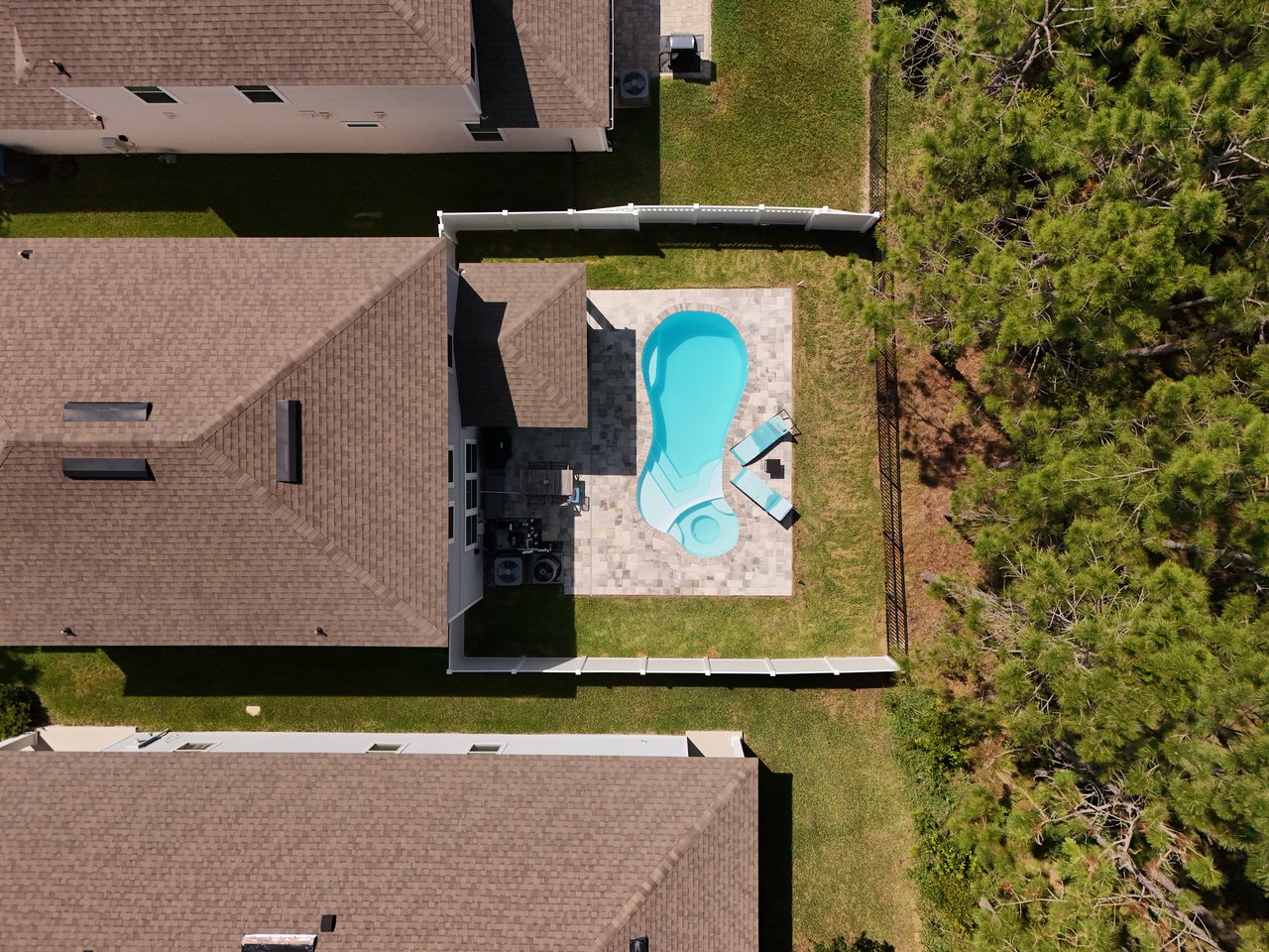 Aerial view of a fenced backyard with a freeform pool, stone patio, and lounge chairs.