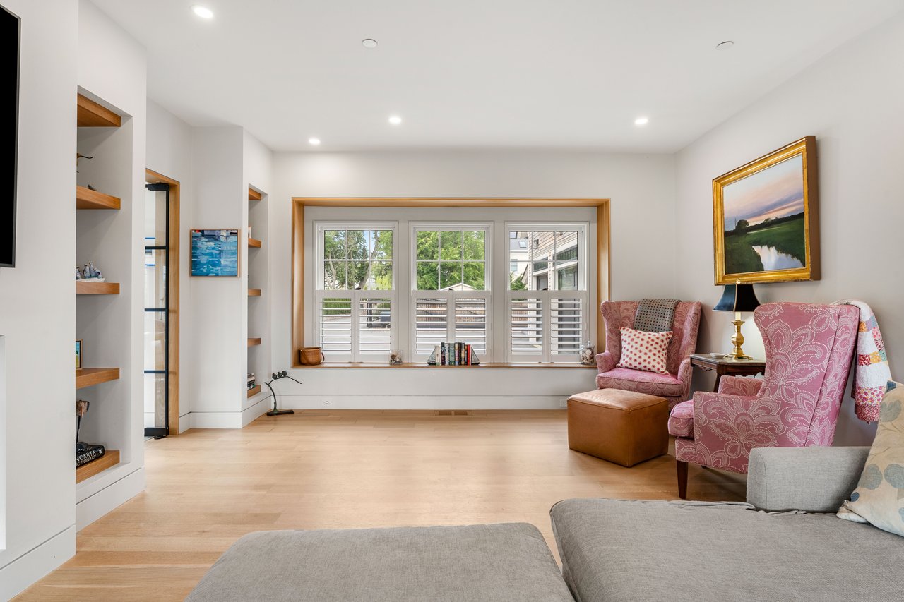 Living room with pale wood floors, built-in shelves, plantation shutters, and pink patterned armchairs.