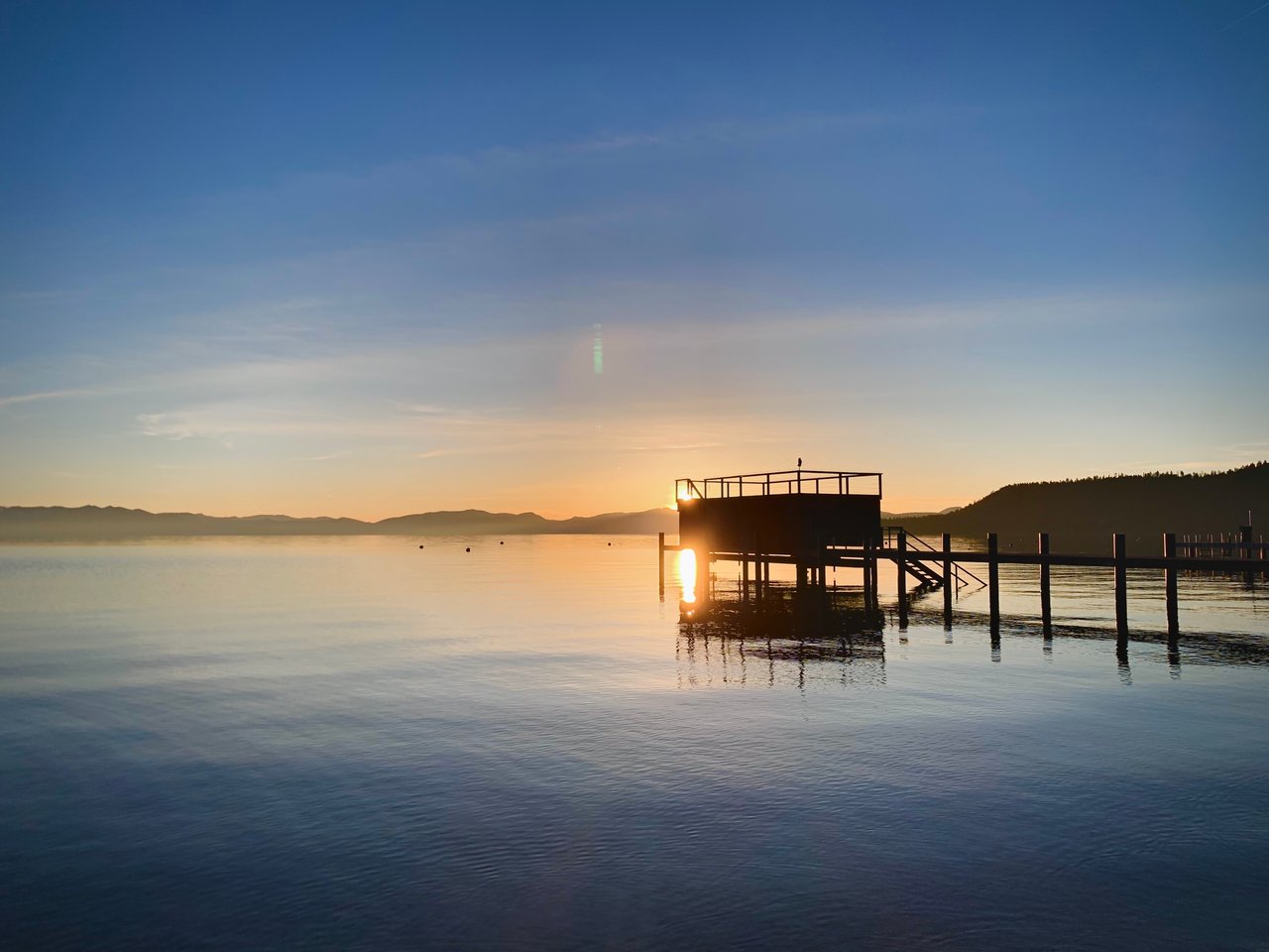A serene sunset view over a private Lake Tahoe pier, illustrating the exclusive lifestyle and beach access that an experienced Incline Village real estate agent helps clients navigate.