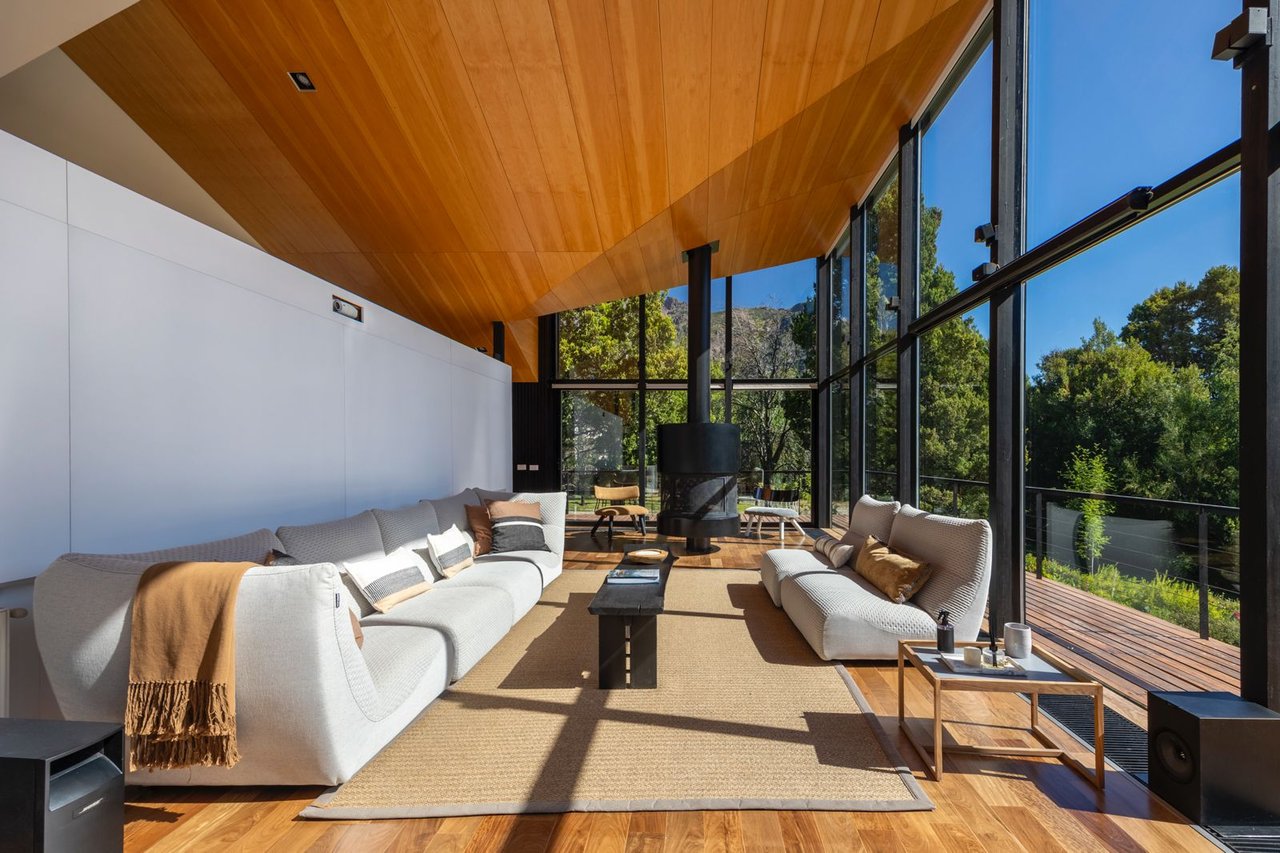 Sunlit living room with a sculptural wood ceiling, glass walls, and forest views.