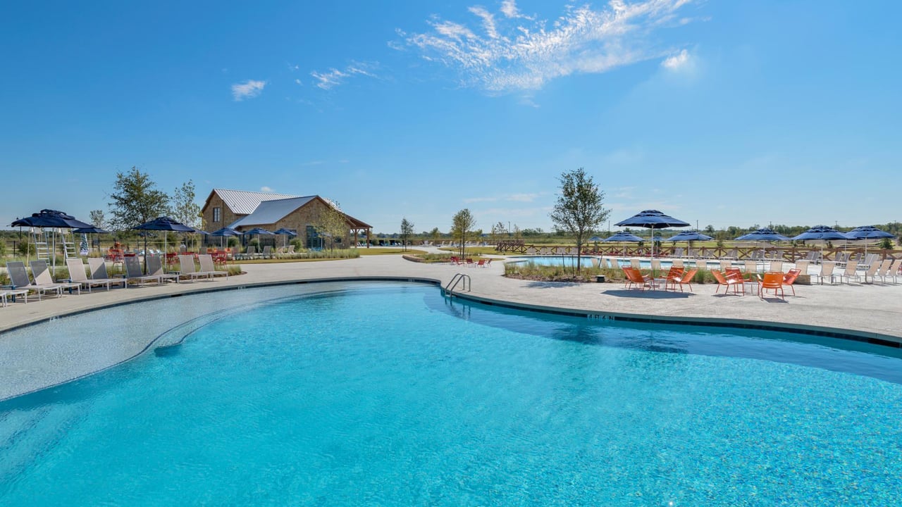 Community pool with turquoise water, shaded lounge chairs, and a stone amenity building.