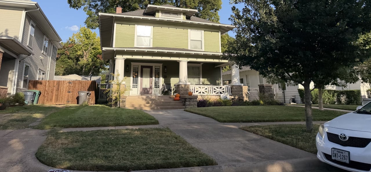 Two-story green home with a broad columned porch and a walkway leading from the sidewalk.