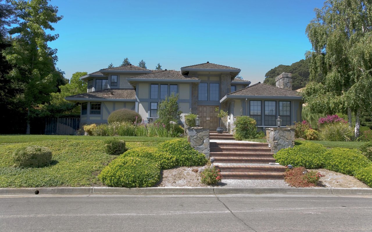 Gray two-story home with a stone entry, tiled steps, and landscaped front garden.