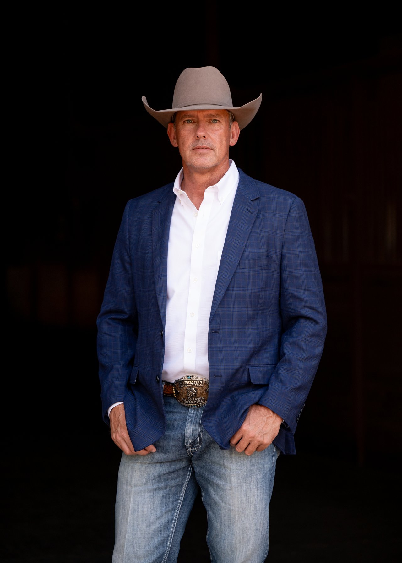 David Inman in a cowboy hat and blue blazer against a dark background.