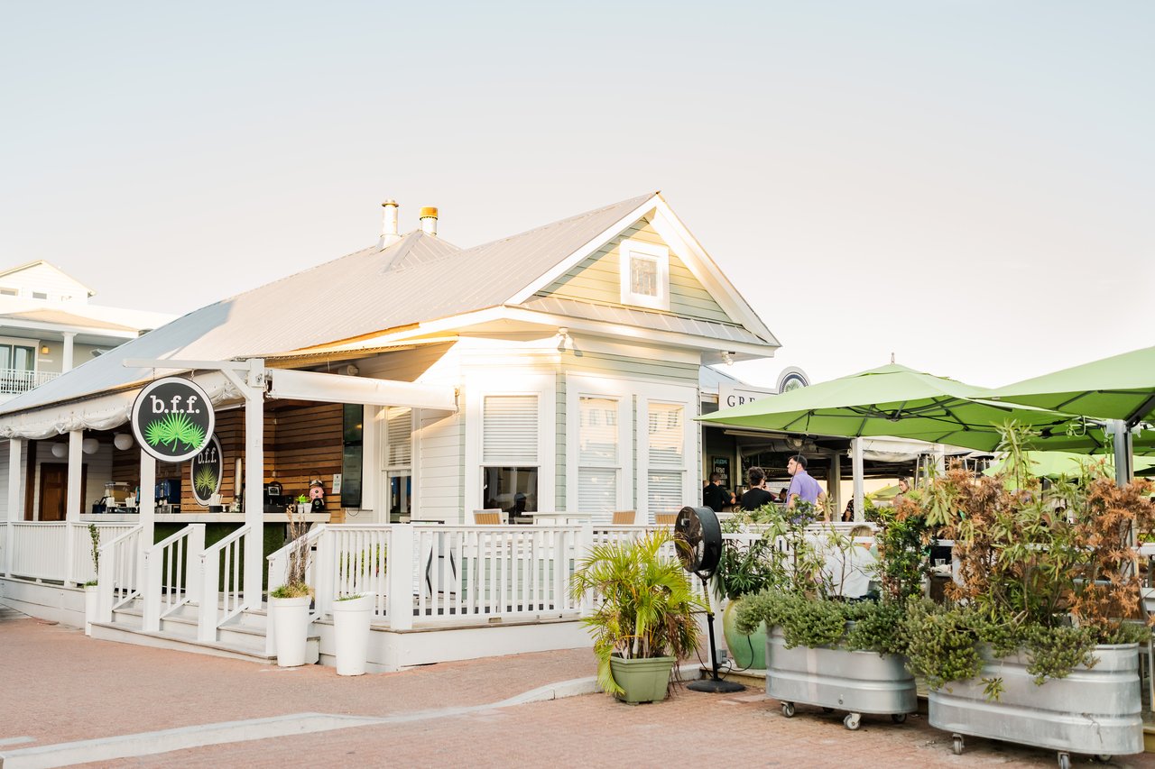 Pale cottage-style Seaside restaurant with a white picket-railed porch and lime-green umbrellas in the town center on 30A, Florida