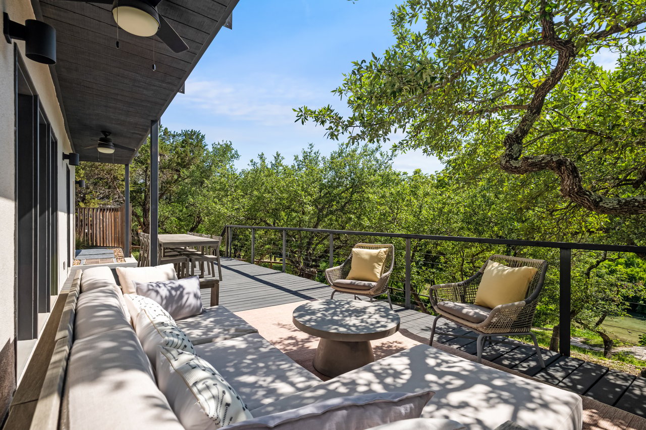 Furnished deck with a gray sectional and woven chairs overlooking leafy trees and a glimpse of water.