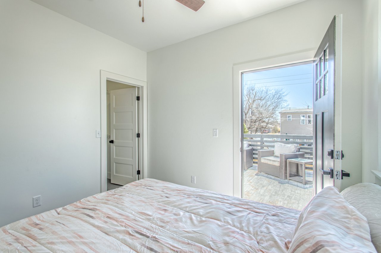 Furnished bedroom with pale striped bedding and an open door to a deck with outdoor seating.