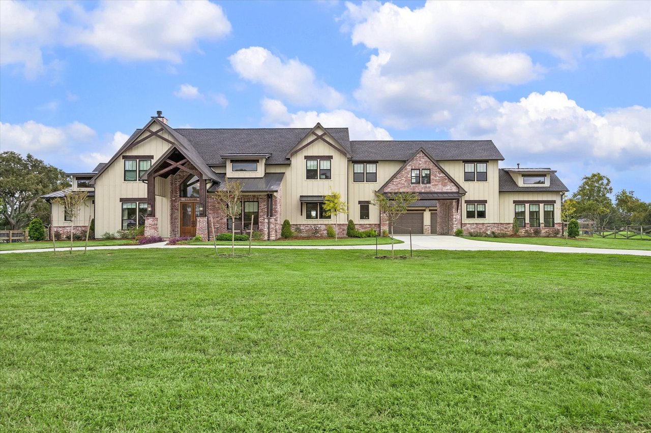 Large two-story home with brick accents, a broad front lawn, and a multi-car garage.