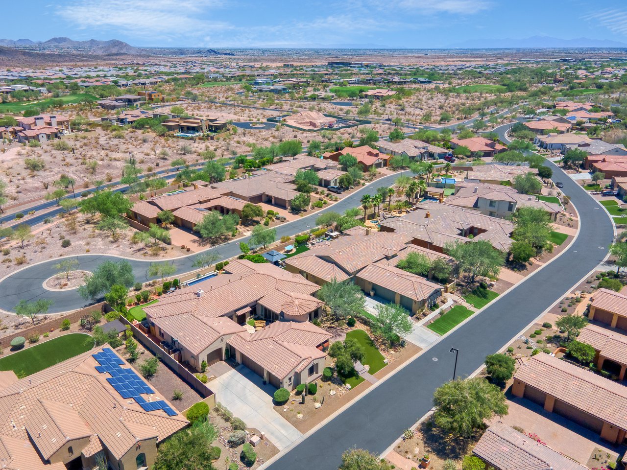 Aerial view of a suburban desert neighborhood with curved streets, single-story homes, and mountains in the distance.