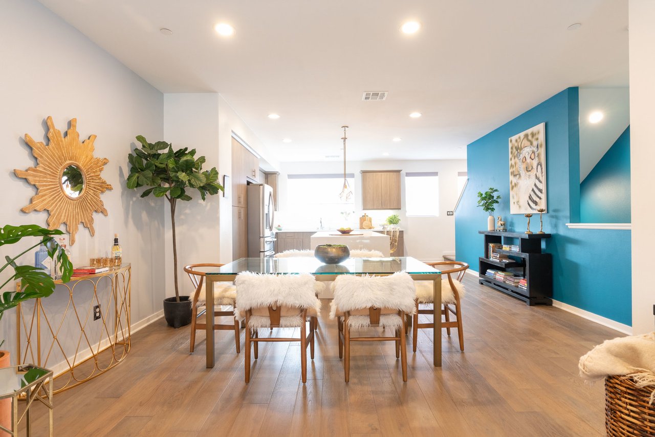 Bright dining area with glass table, wood chairs, blue accent wall, and modern decor, open to kitchen and living space.