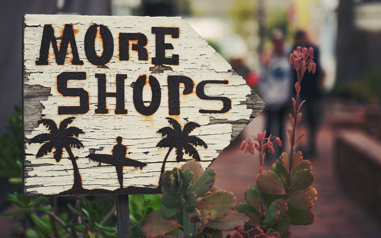 A rustic wooden sign with a palm tree and surfer art points the way to more shops.