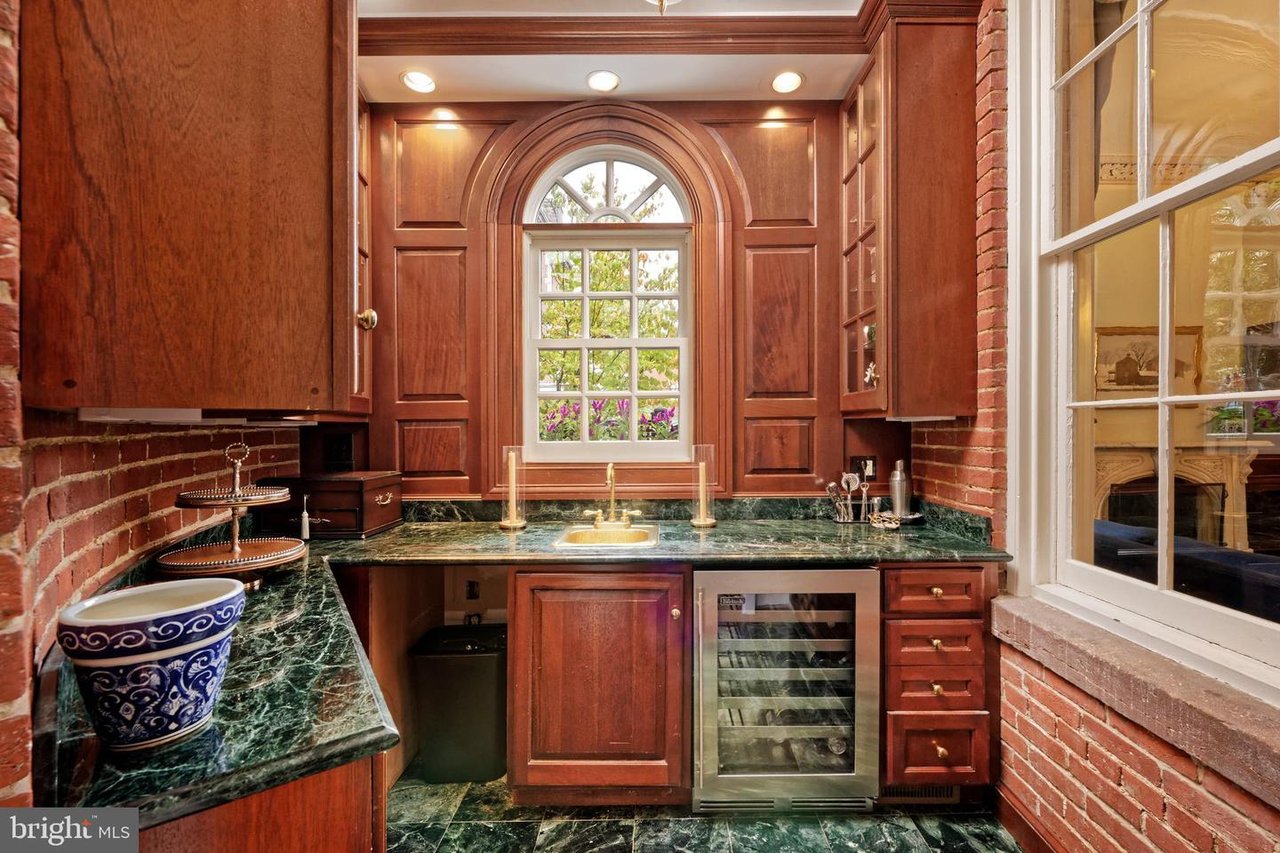 Kitchen with green marble counters, cherry cabinetry, exposed brick, and an arched window above the sink.