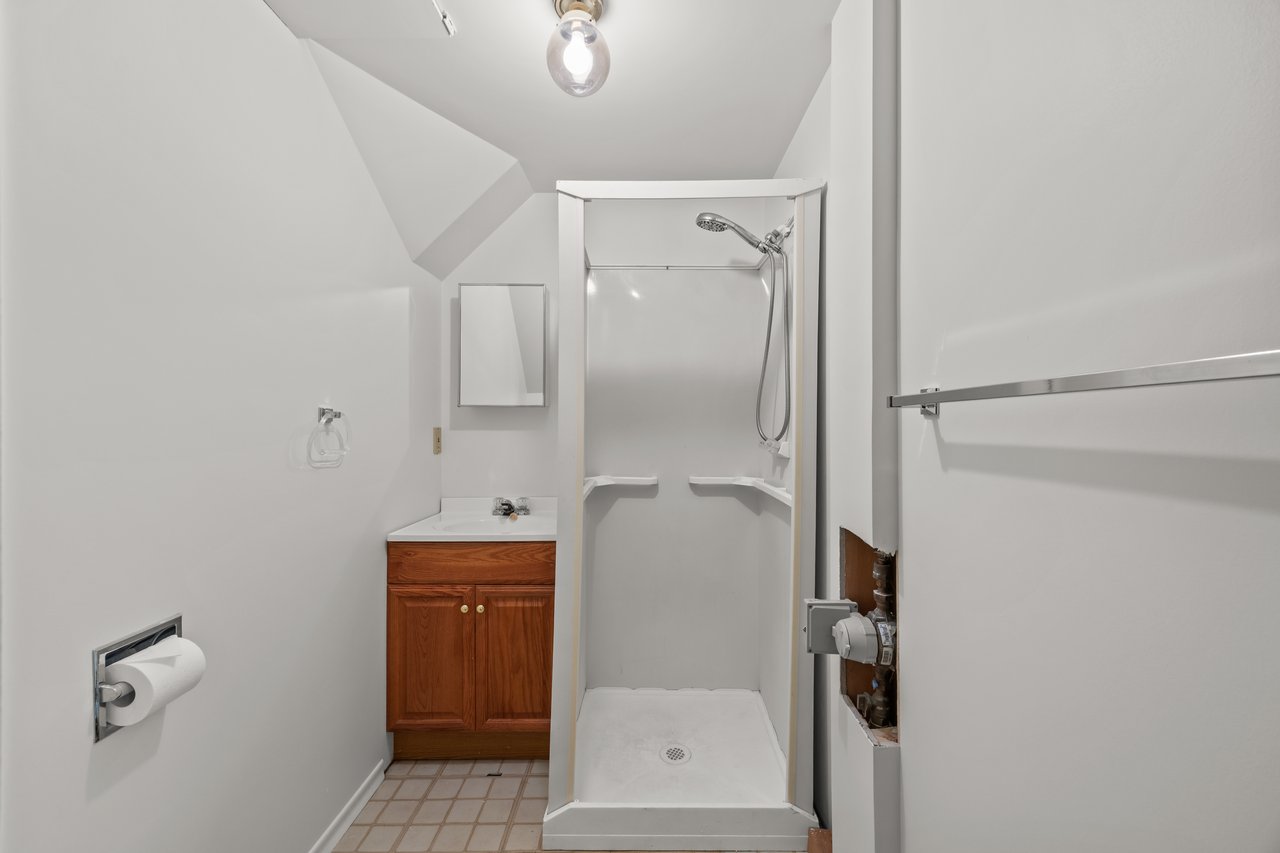 Bathroom with a white corner shower, handheld showerhead, and reddish wood vanity.