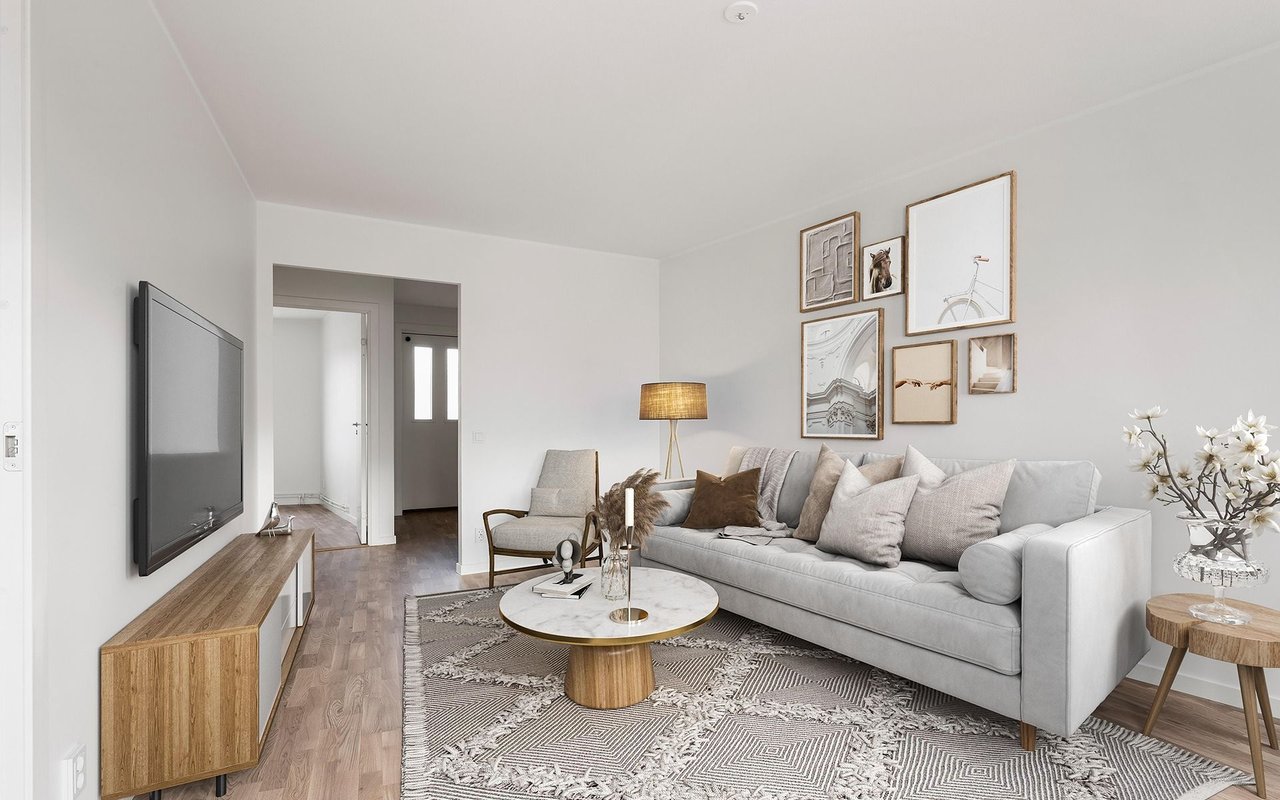 Staged living room with a gray sofa, patterned rug, round coffee table, and wall-mounted television.