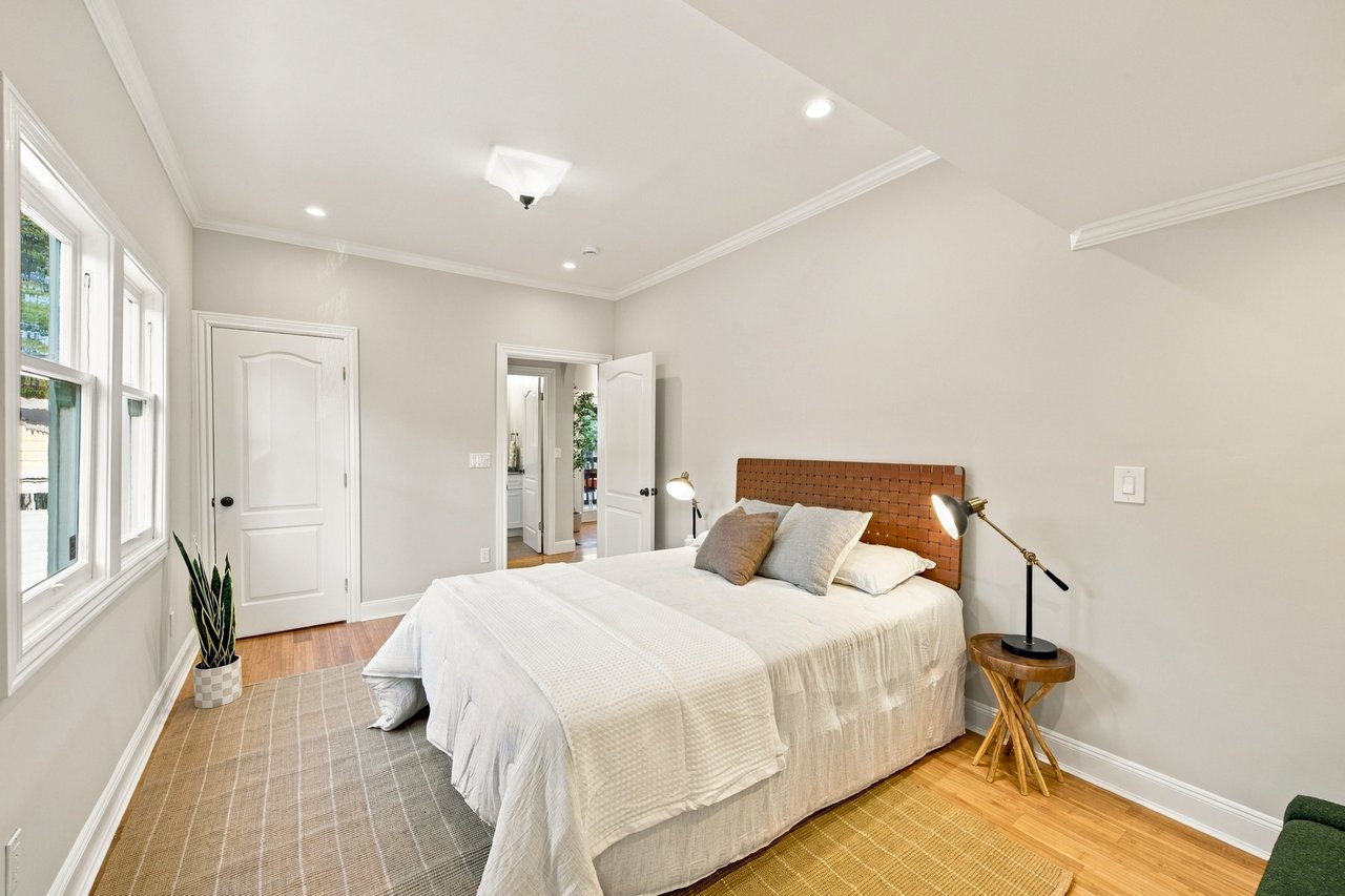 Bedroom with a large bed, wooden headboard, tall windows, and hardwood floors.