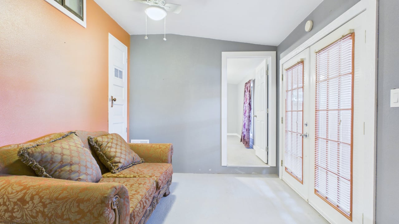 Sitting room with a patterned sofa, gray walls, and glass doors with blinds.